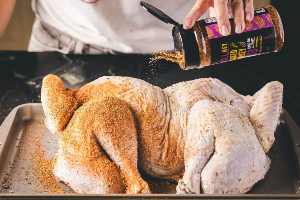 A turkey on a baking sheet being seasoned.