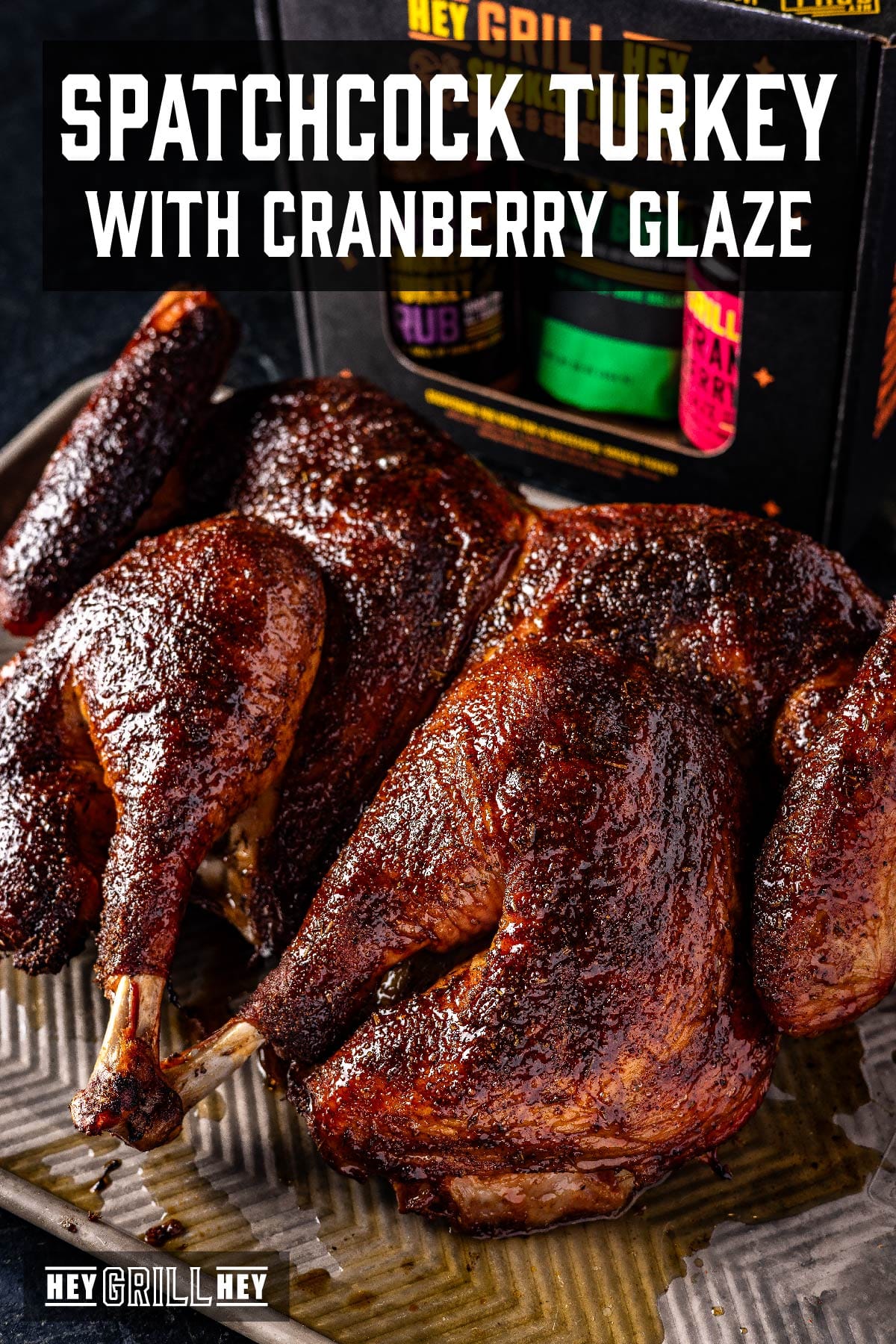 A smoked spatchcock turkey on a baking sheet. The text overlay reads "Spatchcock Turkey with Cranberry Glaze" at the top, and "Hey Grill Hey" at the bottom.