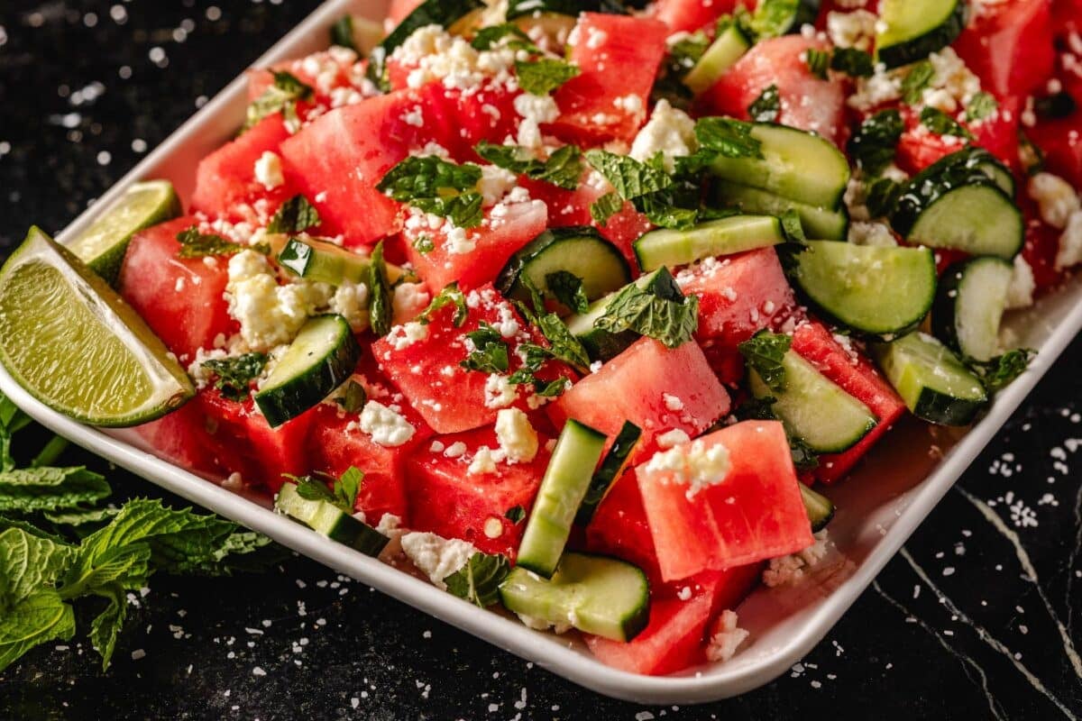 Watermelon and cucumber slices on a platter with a lime wedge on the side.