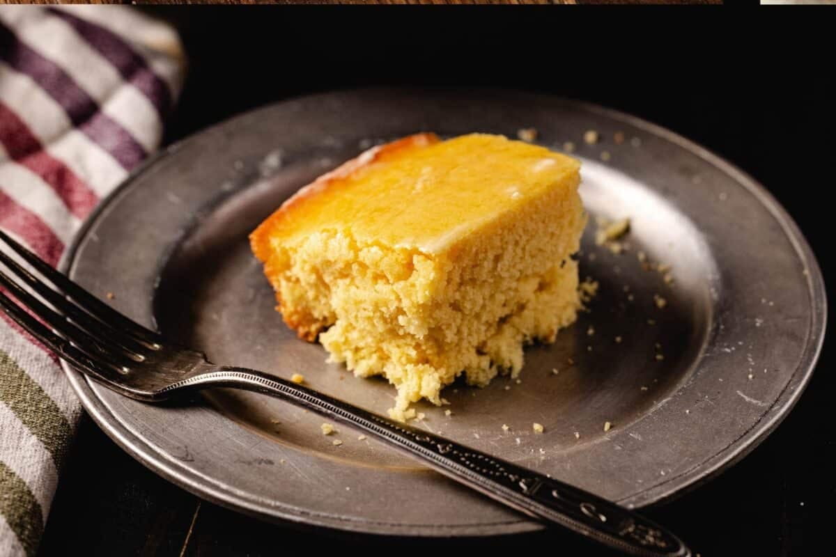 A square slice of cornbread on a metal plate with a fork next to it.