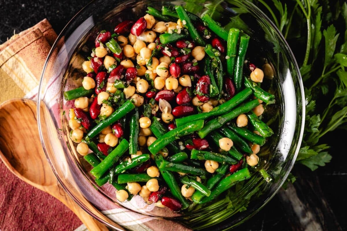 Three bean salad in a glass bowl next to a wooden spoon.