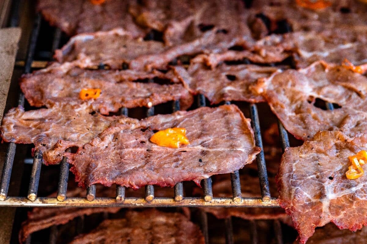 Jerky slices drying on smoker grates, topped with habanero chilis.