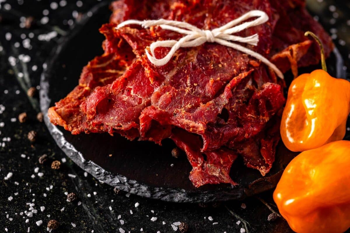 Jerky tied with butcher's twine sitting on a black platter next to habanero peppers.