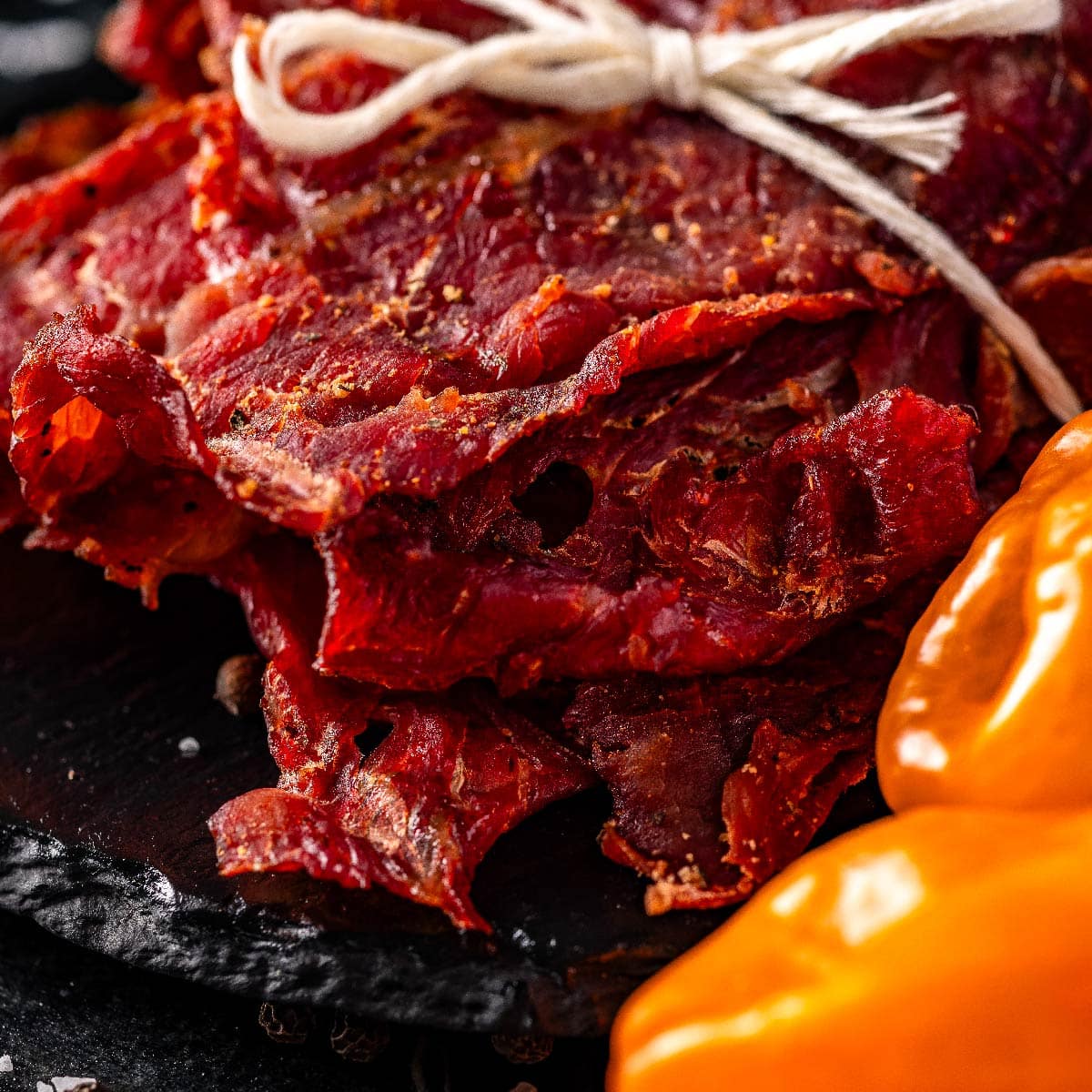 Jerky tied with butcher's twine sitting on a black platter next to habanero peppers.