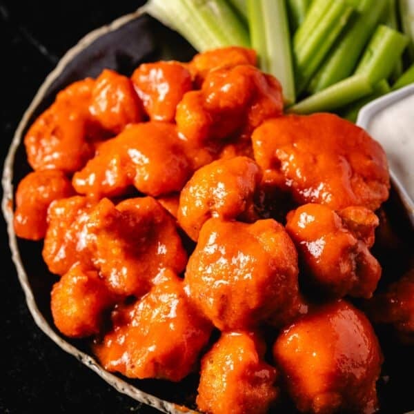 Cauliflower florets in sauce on a plate with a side of ranch dressing and celery sticks.