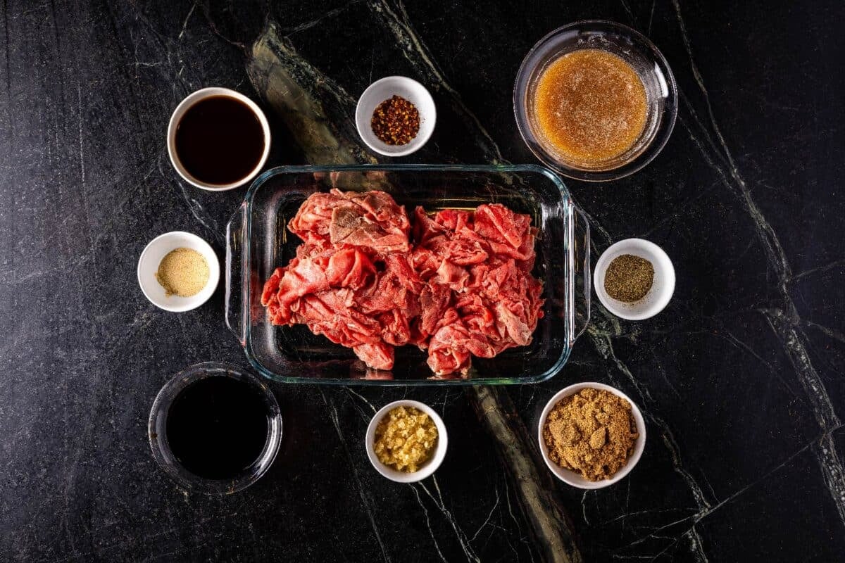 Sliced beef in a baking dish, and glass bowls of marinade ingredients.