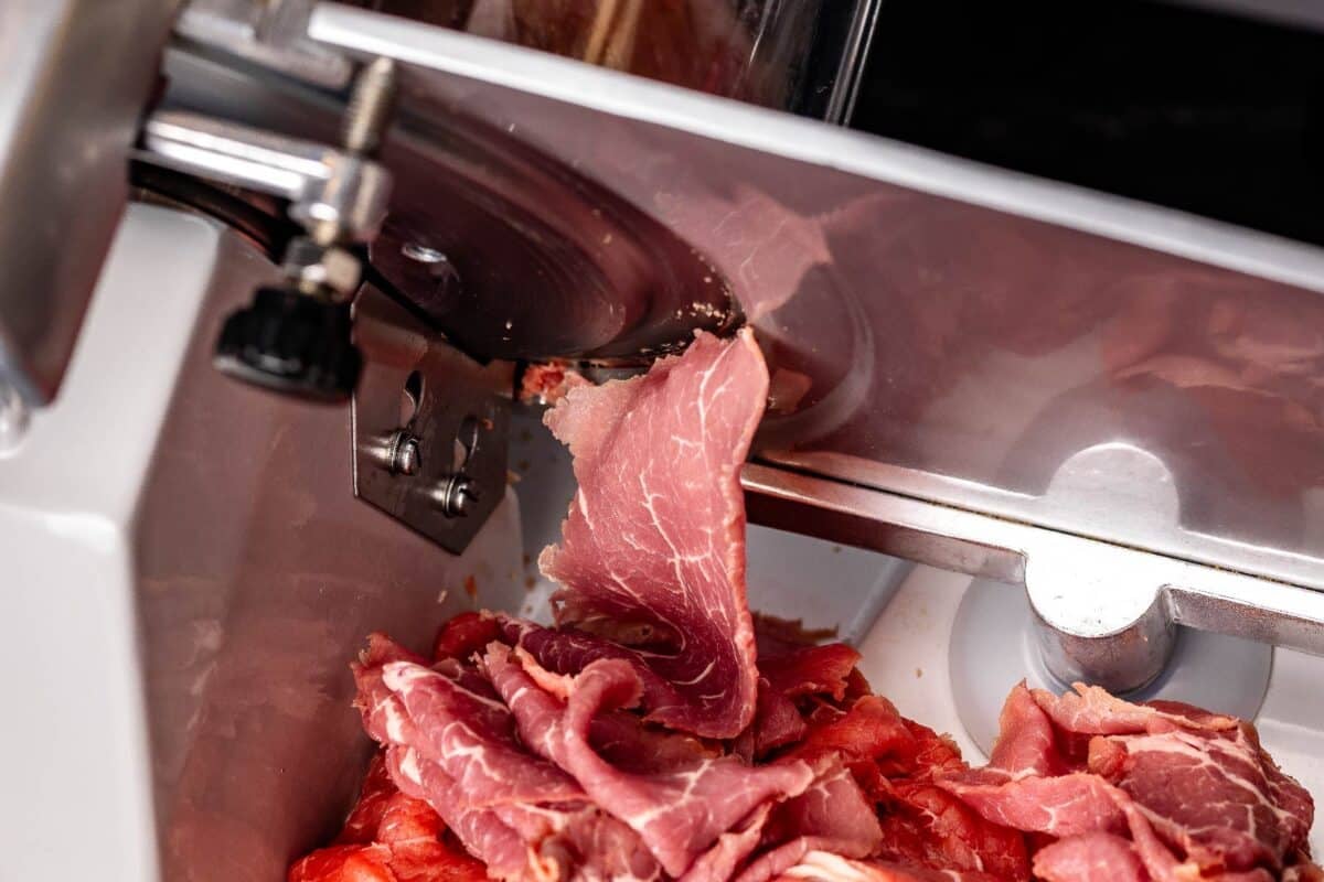 Beef being cut into a pile with a meat slicer.