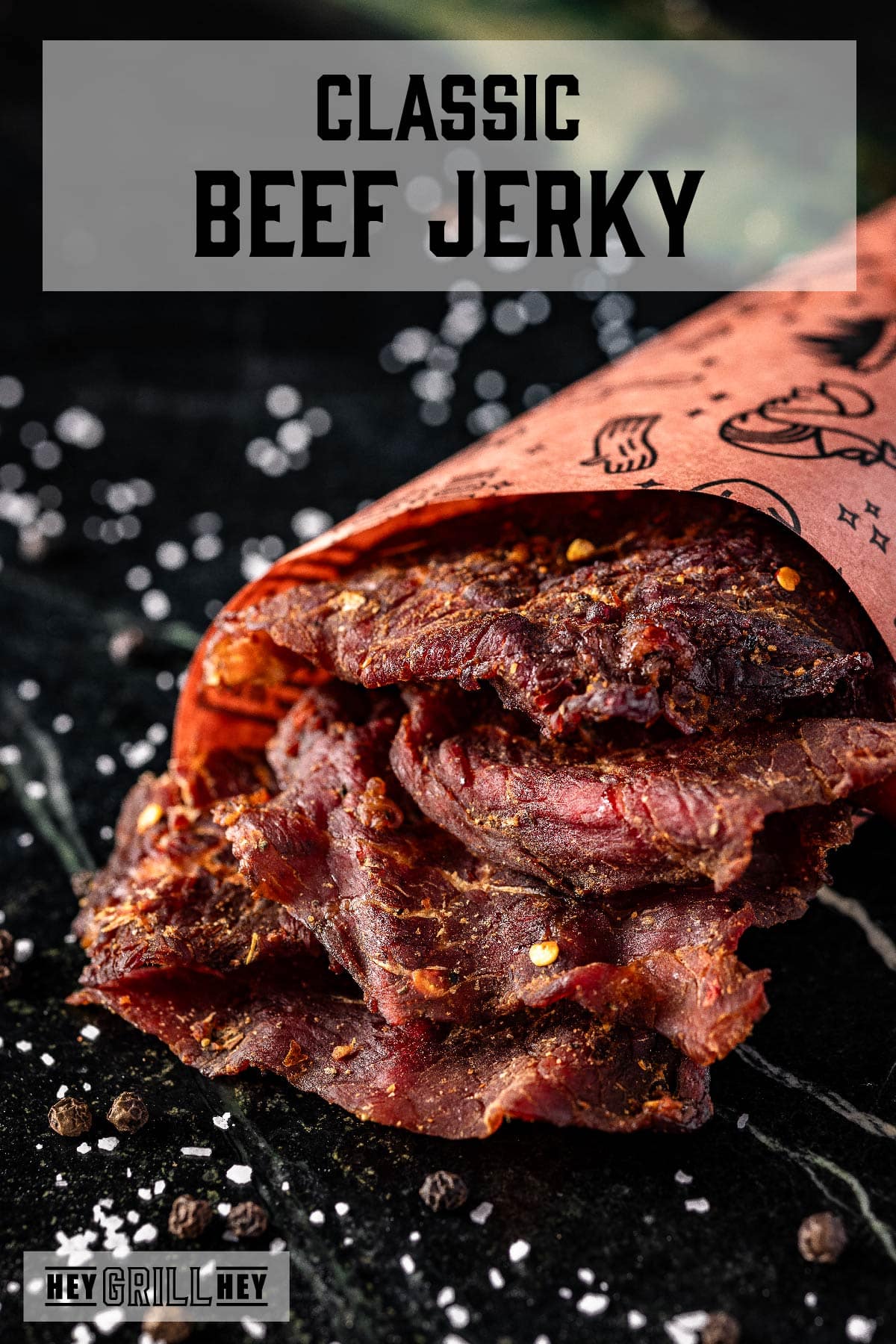 Beef jerky wrapped in paper on a countertop sprinkled with salt. The text overlay reads "Classic Beef Jerky" at the top, and "Hey Grill Hey" at the bottom.