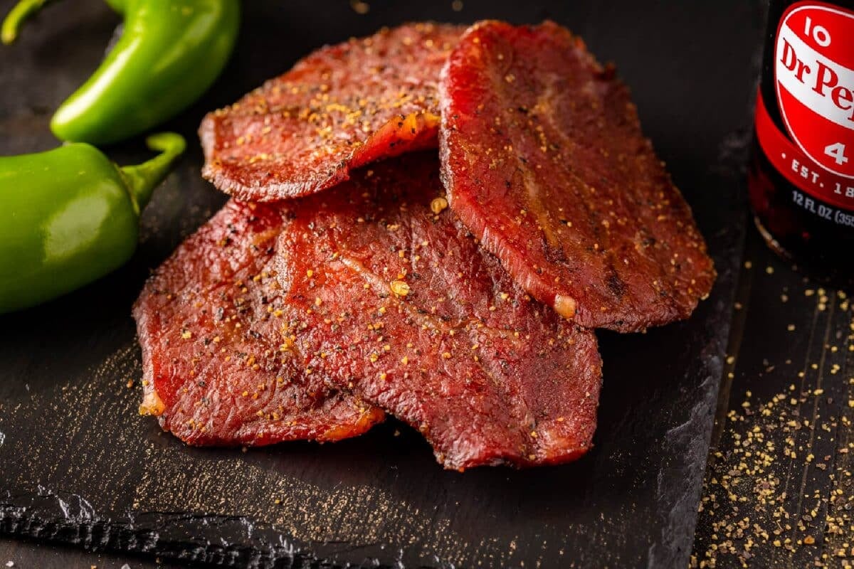 Slices of jerky piled between fresh jalapeños and a bottle of soda.