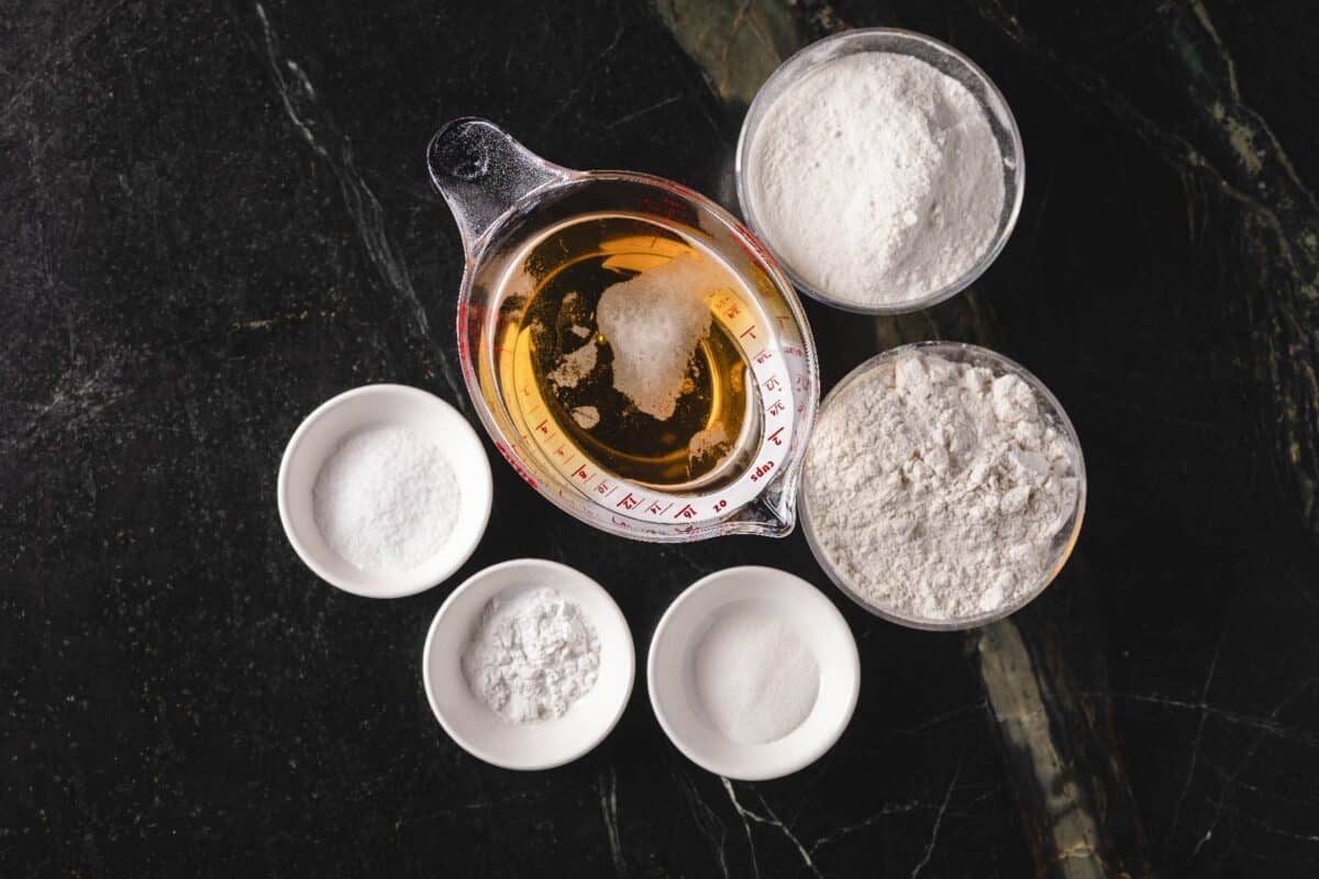 Beer in a measuring cup, and flour and other ingredients in bowls on a countertop.