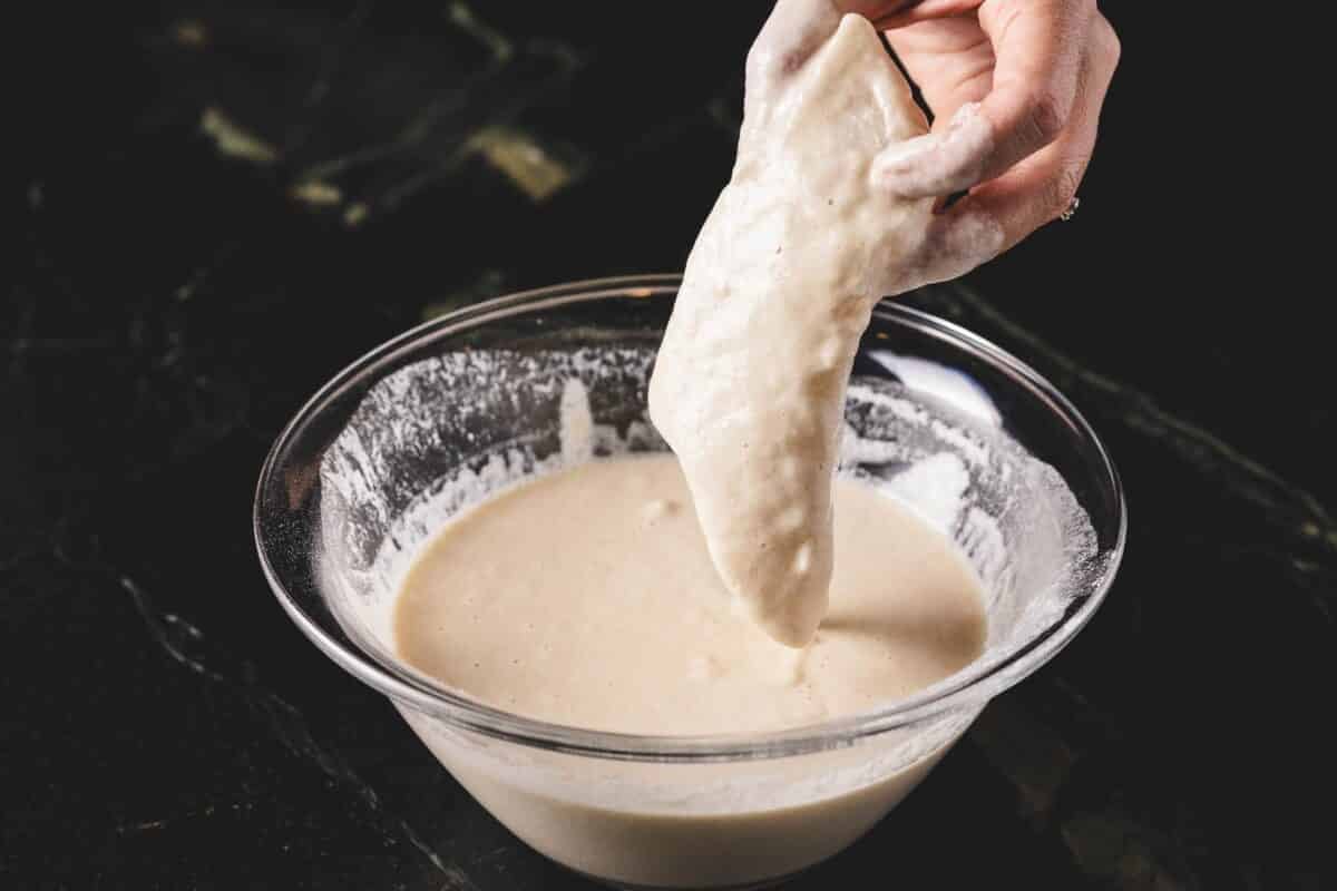 A hand dipping a fillet in a bowl full of batter.