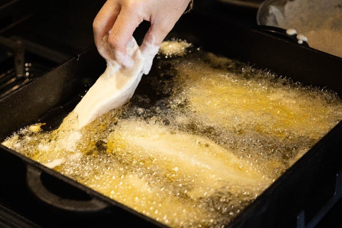 Fish fillets frying in a pan of cooking oil.