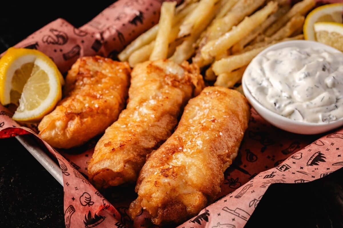 A paper-lined basket filled with fried fish and chips, lemon wedges, and a cup of tartar sauce.