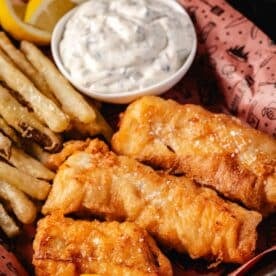 Fish and chips next to a cup of tartar sauce in a basket.