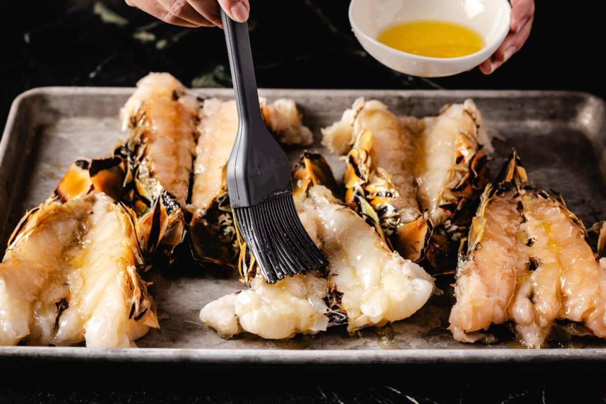 Lobster rolls on a baking sheet being brushed with butter.