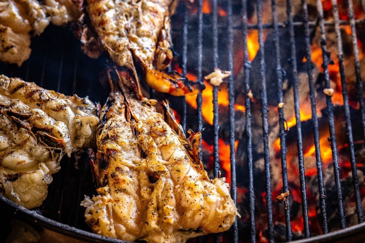 Lobster tails sitting on grill grates over hot charcoals.