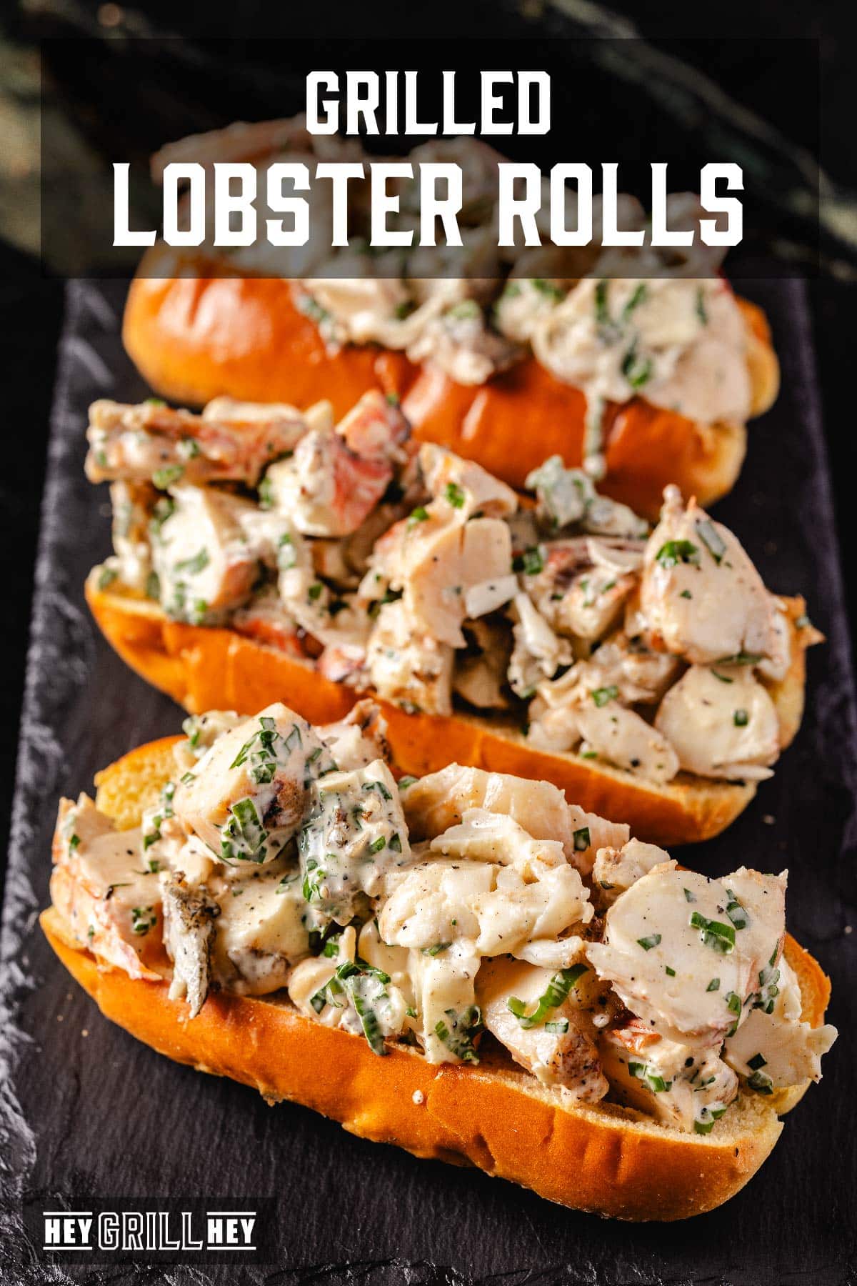 Three lobster rolls on a black platter. The text overlay reads "Grilled Lobster Rolls" at the top, and "Hey Grill Hey" at the bottom.