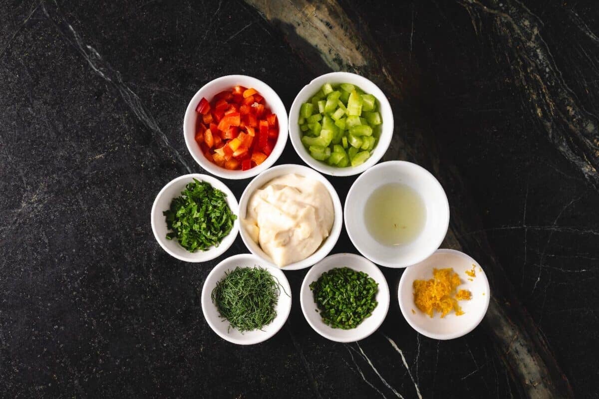 Diced bell peppers and celery, mayo, and other seasonings in glass bowls on a countertop.