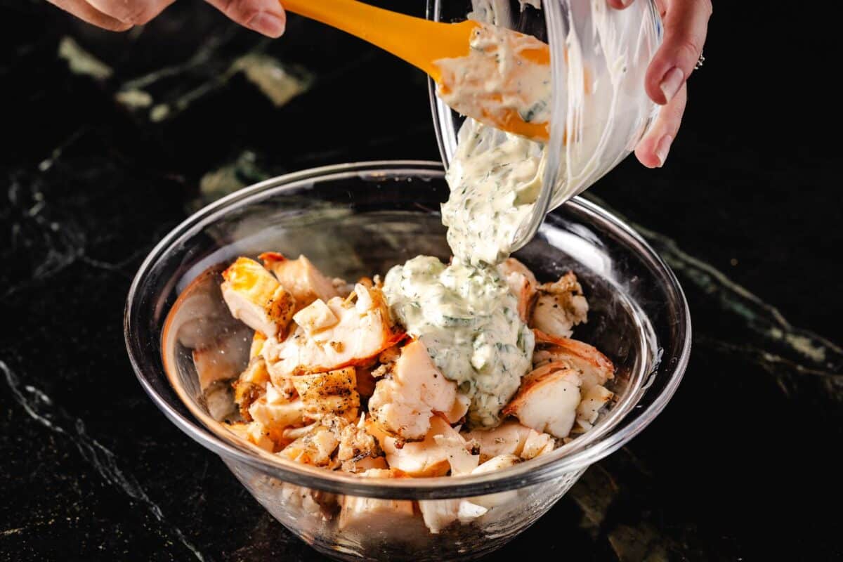 Salad dressing being dumped onto lobster in a bowl.