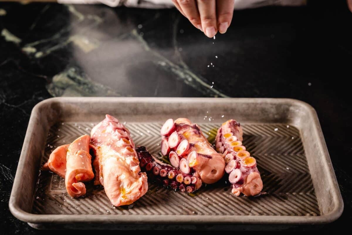 Braised octopus on a baking sheeting being seasoned for the grill.