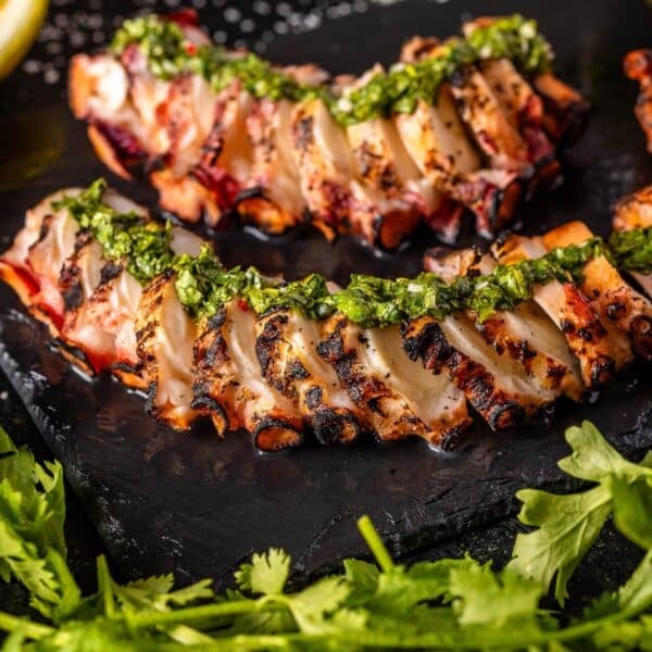 Sliced octopus on a black platter topped with chimichurri sauce.