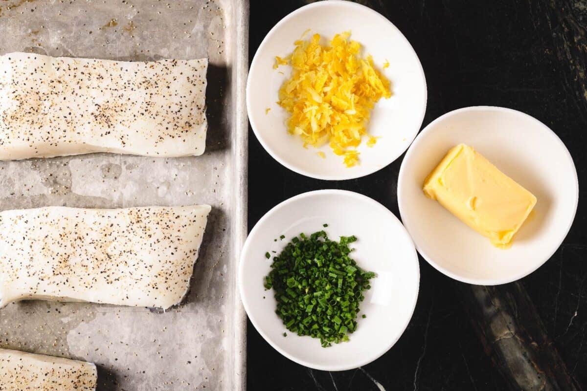 Sea bass fillets on a baking sheet next to bowls on butter, chives, and lemon zest.