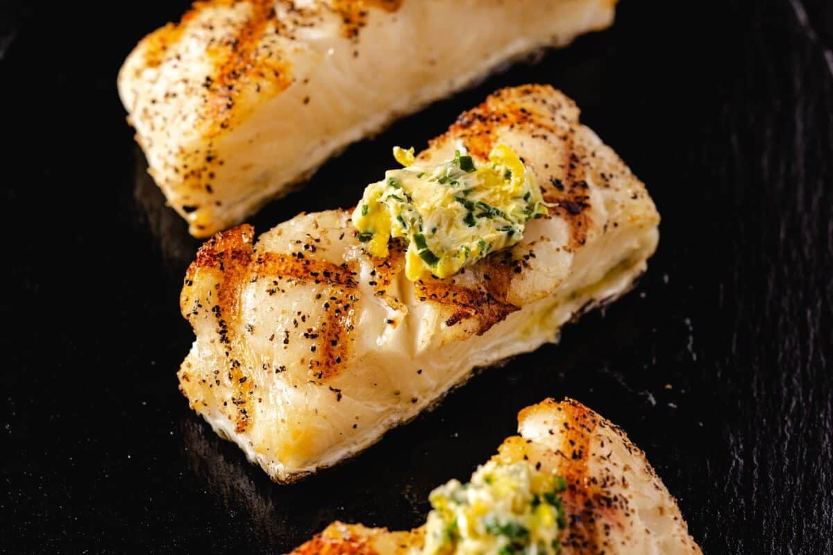 Grilled sea bass fillets on a black plate.