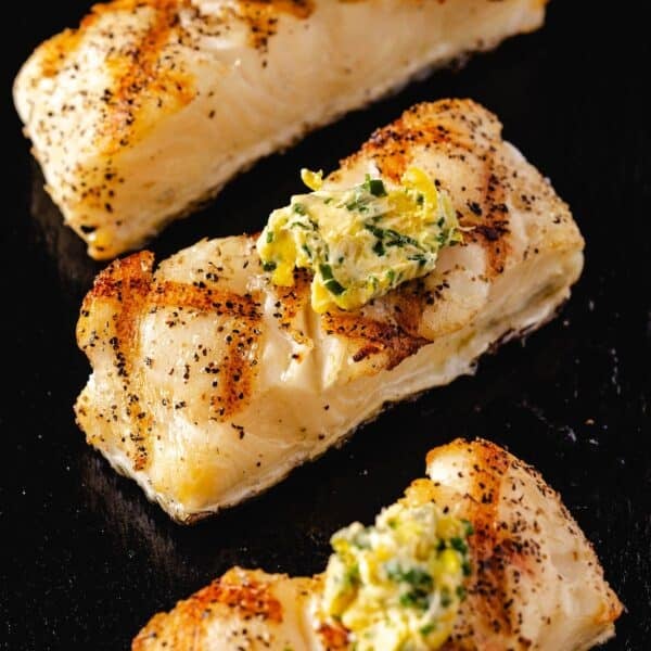 Grilled sea bass fillets topped with butter and lemon zest on a black plate.