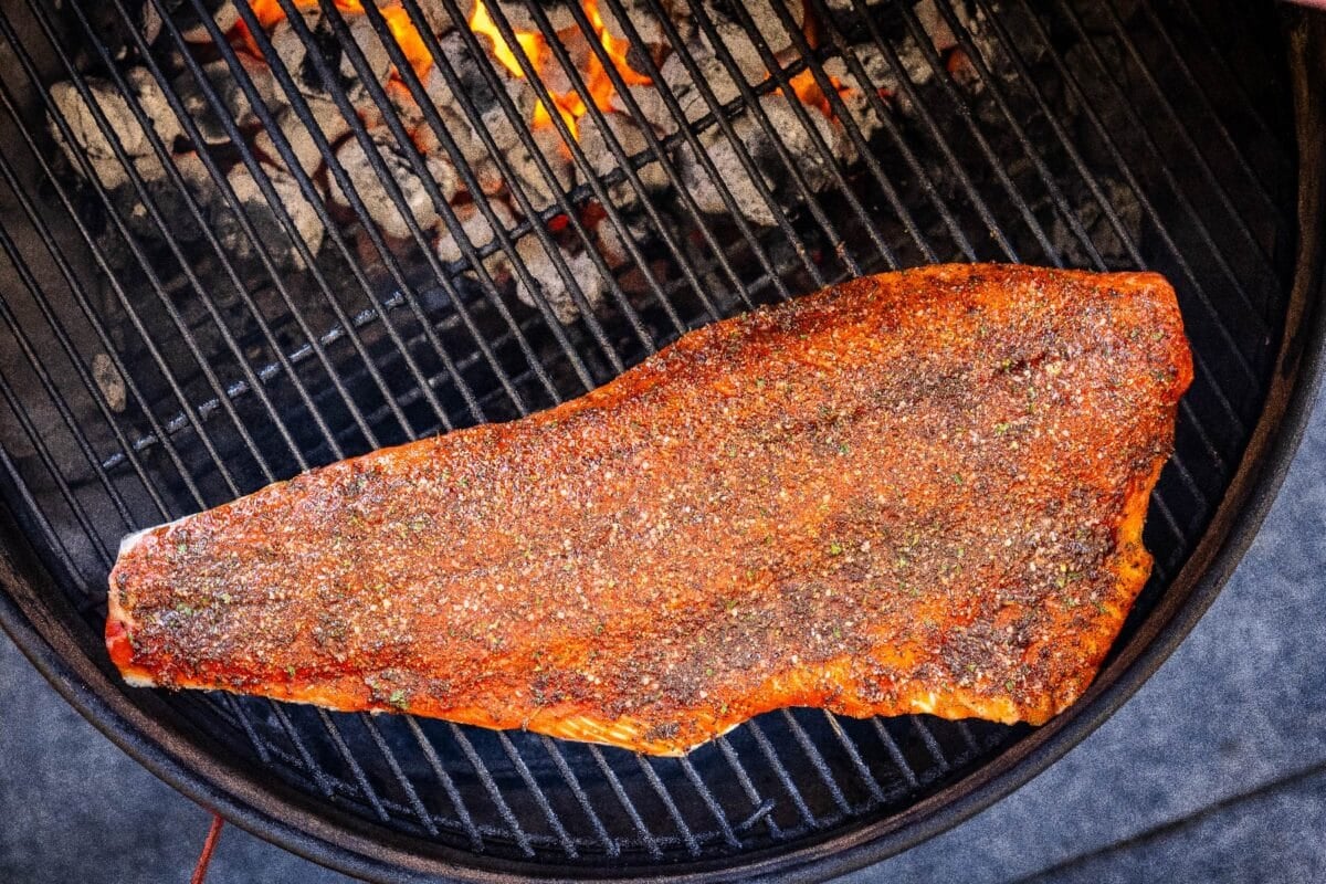 A steelhead trout fillet on grill grates over charcoals.