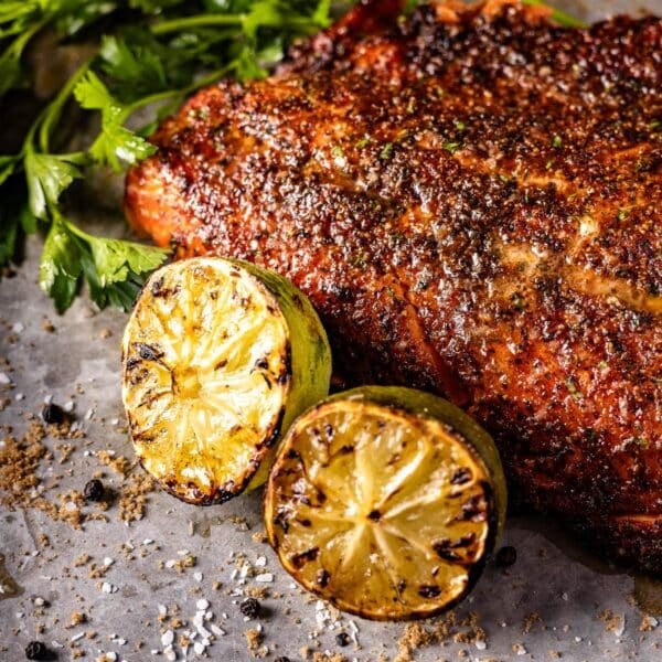 Grilled steelhead trout on a serving dish with lime halves and garnish.