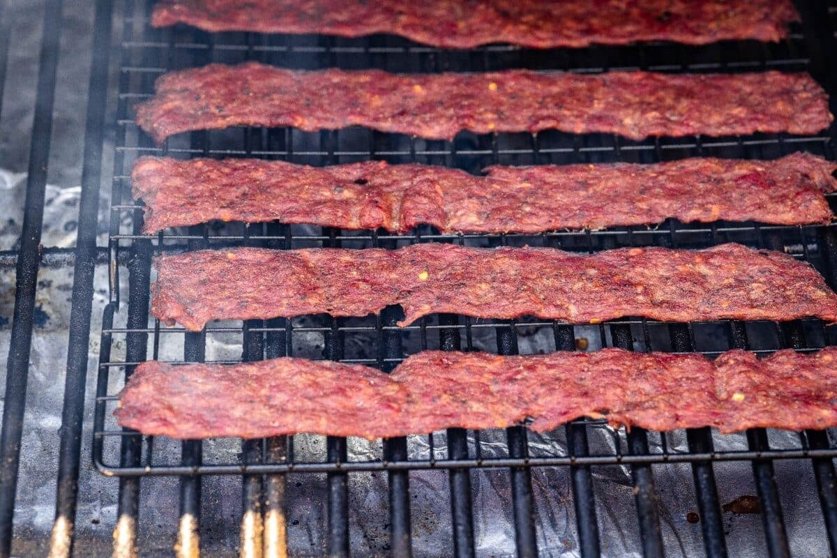 Venison jerky strips drying on smoker grates.