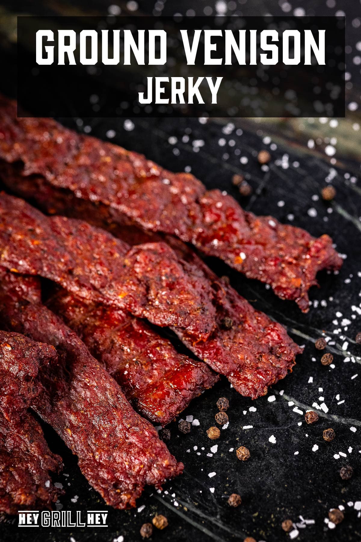 Jerky sticks on a black plate. The text overlay reads "Ground Venison Jerky" at the top, and "Hey Grill Hey" at the bottom.