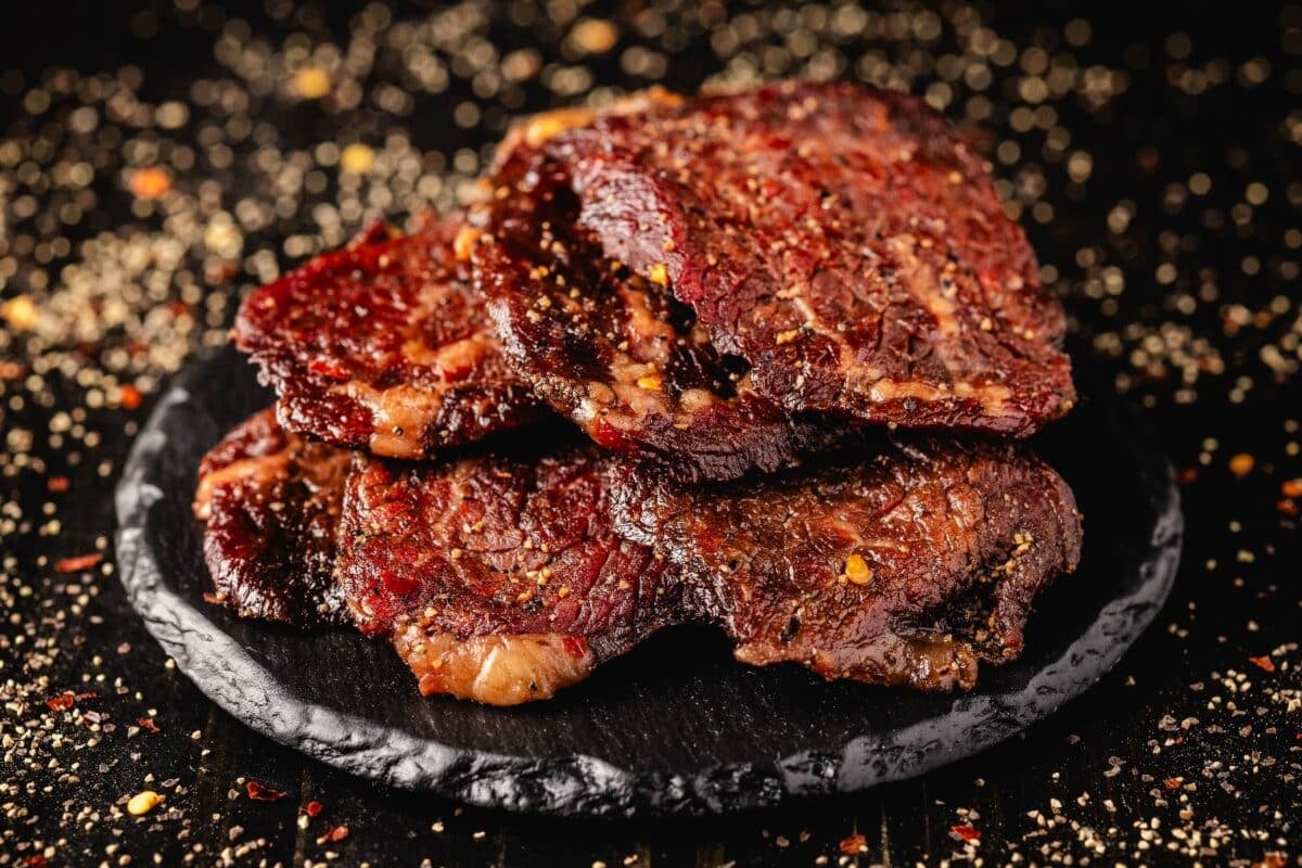 Peppered beef jerky on a black plate.