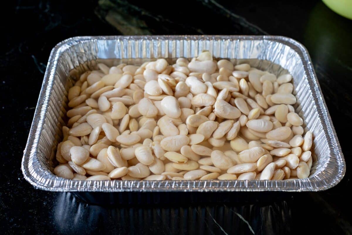 Beans soaking in water in an aluminum pan.