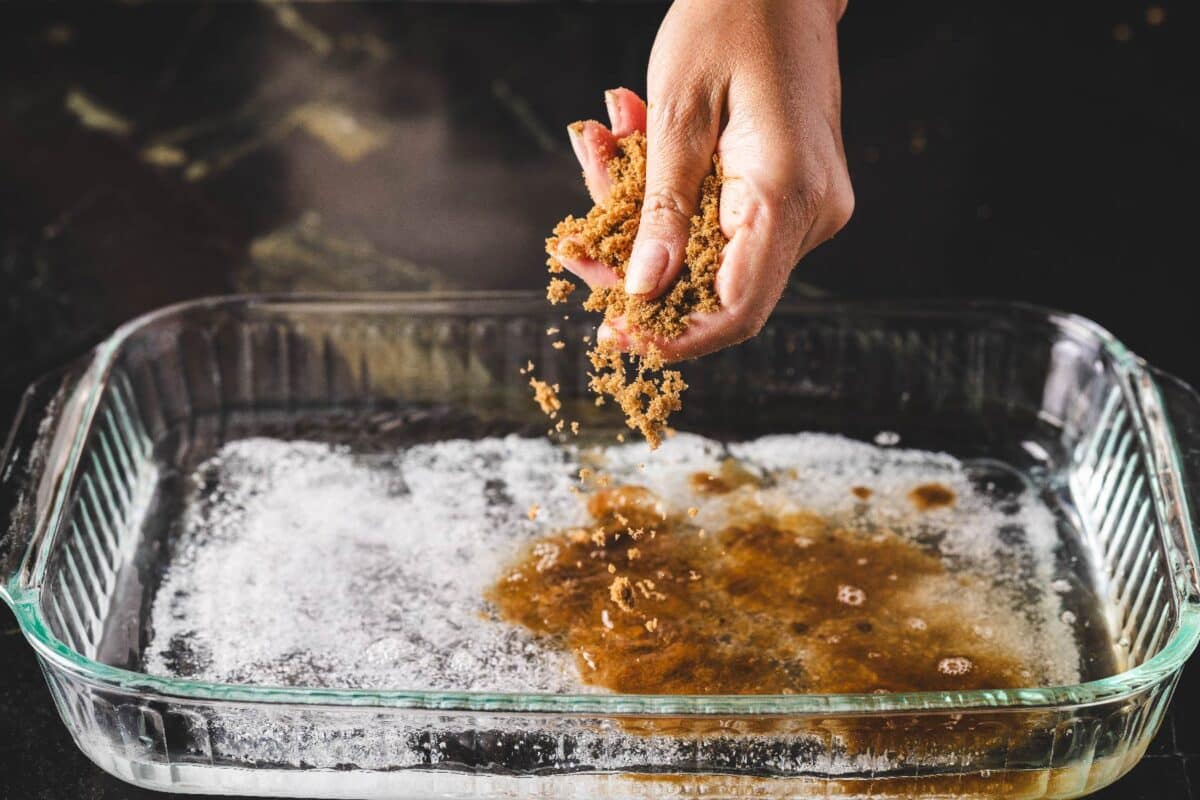 A baking dish lined with a layer of salt being sprinkled with brown sugar.