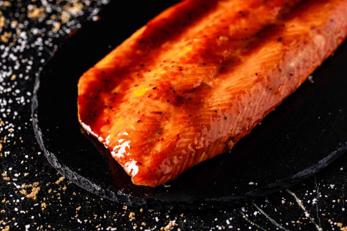 Smoked steelhead trout on a black serving platter sprinkled with salt and brown sugar.