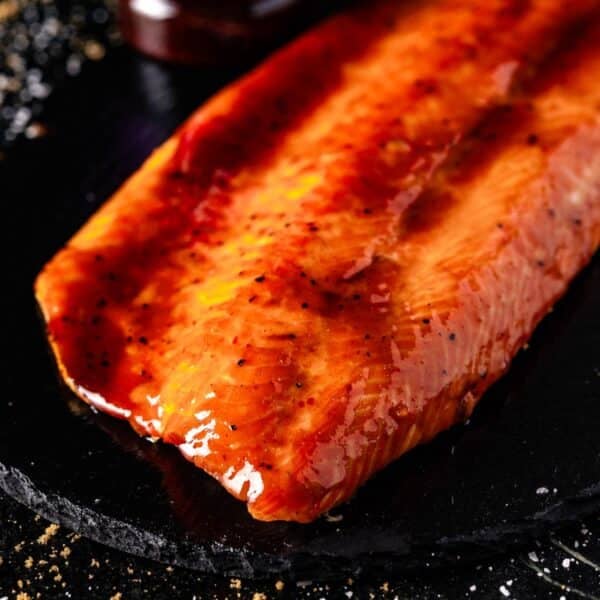 Glazed steelhead trout on a black plate.