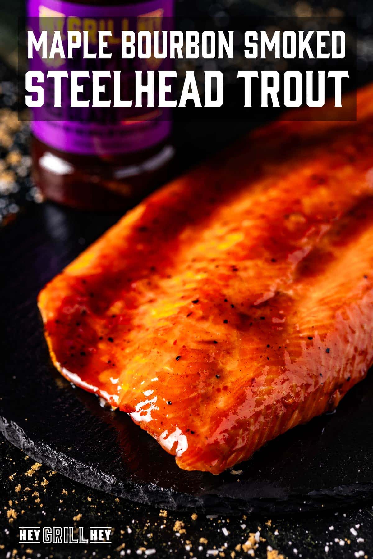 A glazed fish fillet on a serving platter. The text overlay reads "Maple Bourbon Smoked Steelhead Trout" at the top, and "Hey Grill Hey" at the bottom.