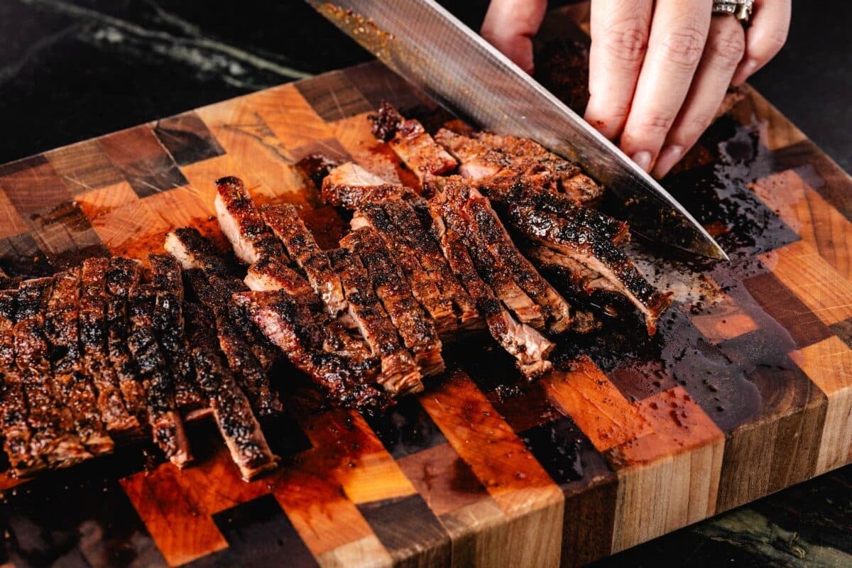 Steak on a wooden cutting board being sliced with a knife.