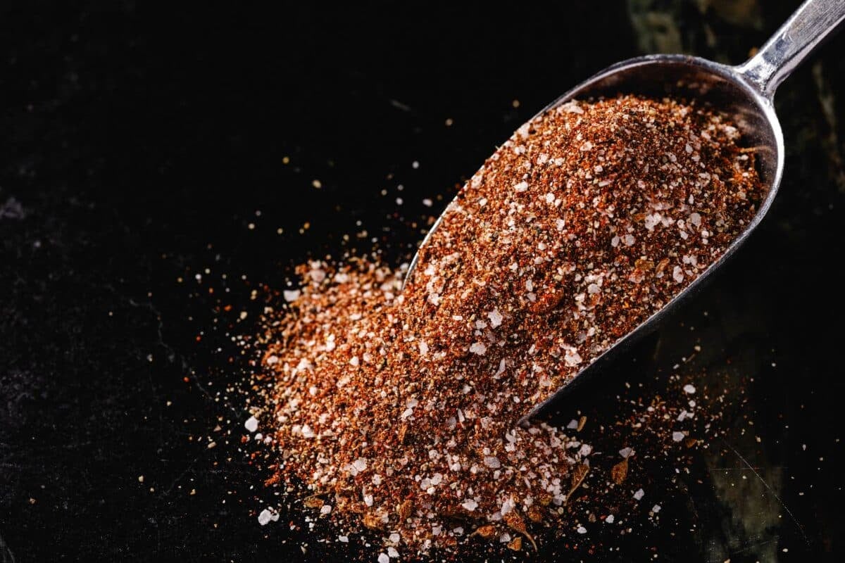 A metal scoop full of BBQ rub spilling onto a countertop.