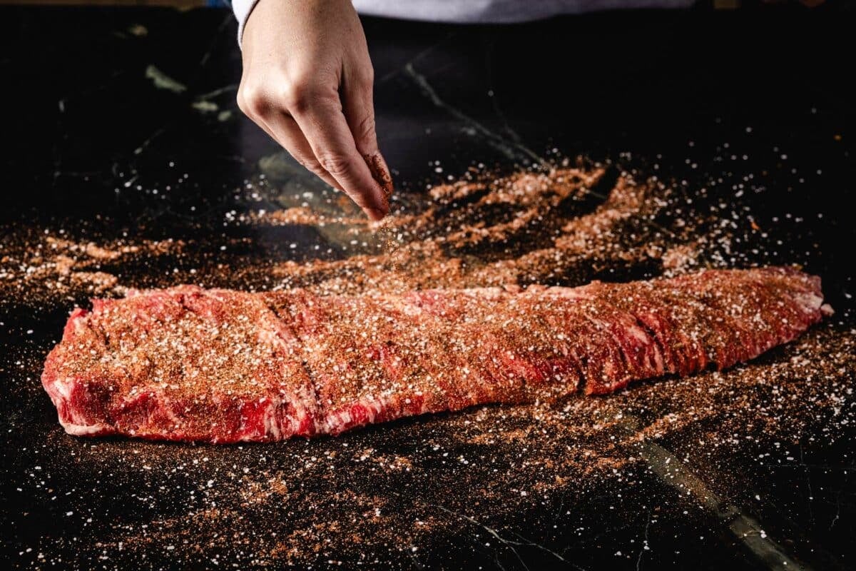 A cut of beef being sprinkled with seasoning.