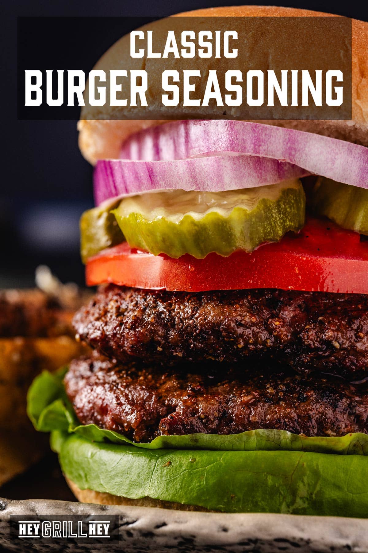 A close up shot of a burger with lettuce, two patties, a tomato slice, pickles, and red onions. The text overlay reads "Classic Burger Seasoning" at the top, and "Hey Grill Hey" at the the bottom.