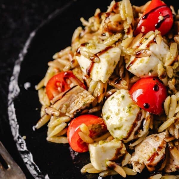 A bowl filled with pasta, tomatoes, and mozzarella balls, sitting on a black stone platter.