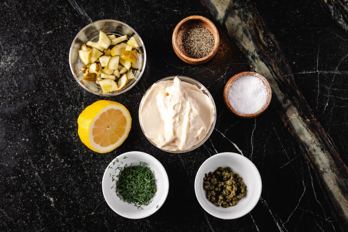 Glass bowls with mayo, dill, and various seasonings on a marble countertop.