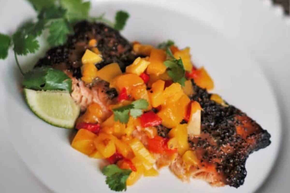 A grilled fish fillet on a white plate topped with mango salsa.