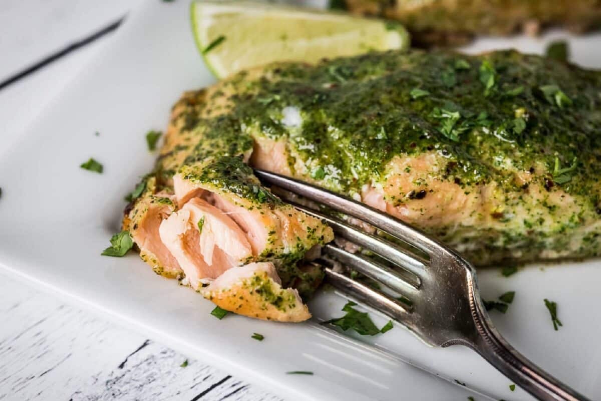 A fork cutting into a salmon fillet with cilantro glaze on a white plate.