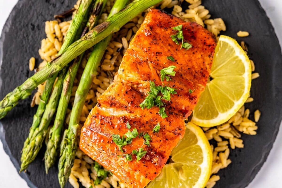 A glazed salmon fillet on a plate with asparagus spears and lemon slices.