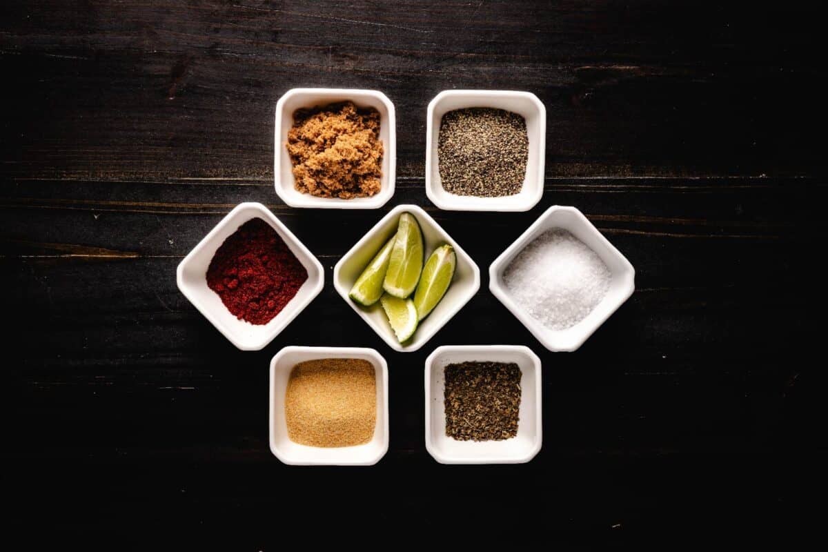 Raw seasoning ingredients in white glass bowls on a tabletop.