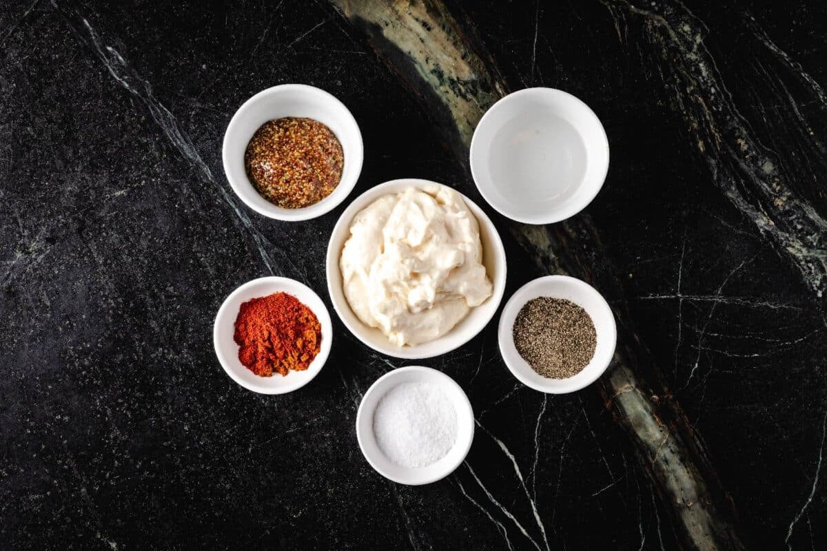 Mayo and various seasonings in glass bowls on a countertop.