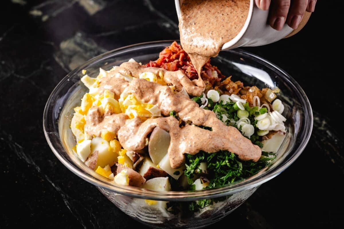 Salad ingredients in a bowl with a cup above pouring on dressing.